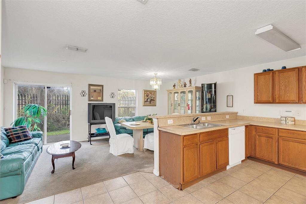 A kitchen with wood cabinets and a tile floor opens to a carpeted living area — 1209 W 6TH STREET, SANFORD, FL