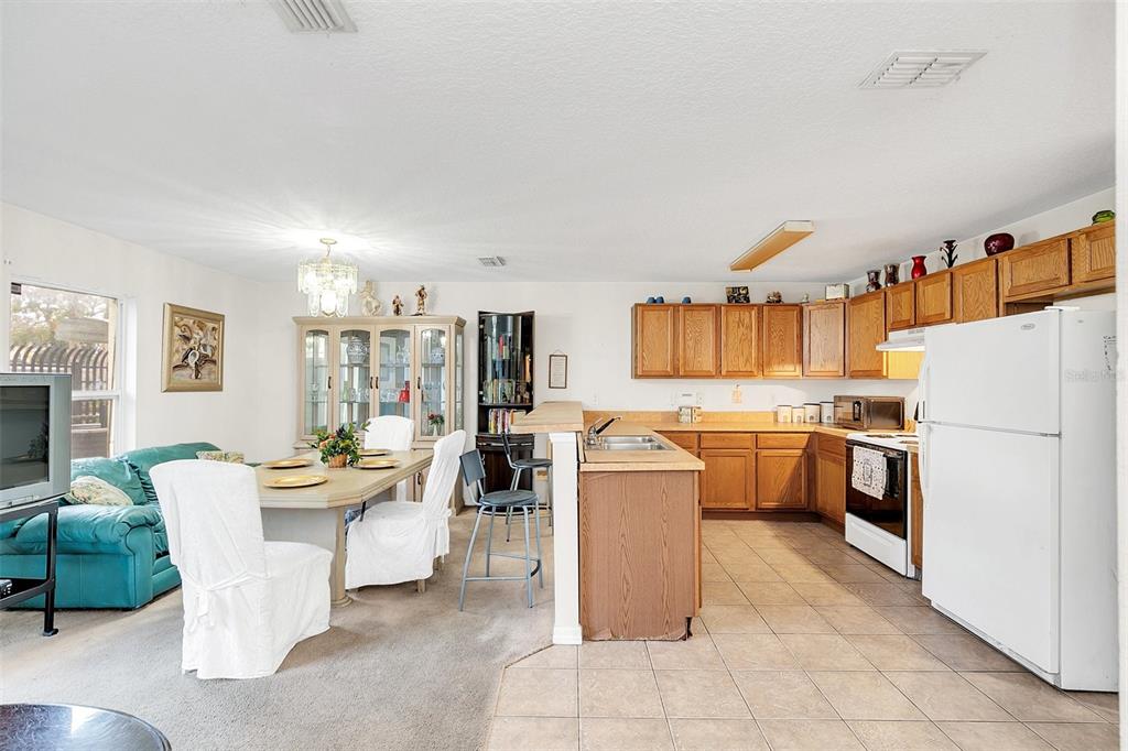 An open-concept kitchen and dining area featuring oak cabinets, tile flooring, and a dining set — 1209 W 6TH STREET, SANFORD, FL