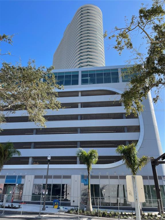 A tall, modern residential tower rises above a multi-level parking garage with ground-floor retail space — 400 CENTRAL AVE UNIT 606, ST PETERSBURG, FL
