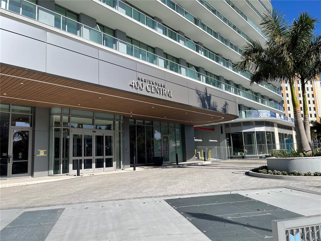 The exterior entrance of a modern high-rise building features glass doors and a curved canopy — 400 CENTRAL AVE UNIT 606, ST PETERSBURG, FL