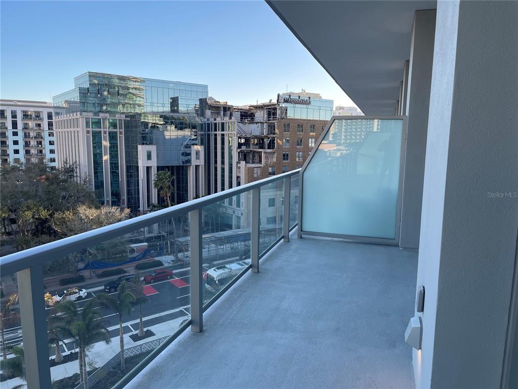 A balcony with a glass railing overlooks a city street and nearby buildings — 400 CENTRAL AVE UNIT 606, ST PETERSBURG, FL