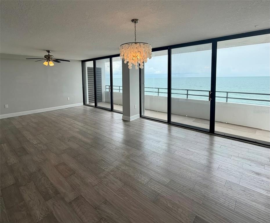 An empty living room features wood-look tile flooring, a chandelier, and sliding doors overlooking the ocean — 1601 N CENTRAL AVENUE UNIT 1101, FLAGLER BEACH, FL