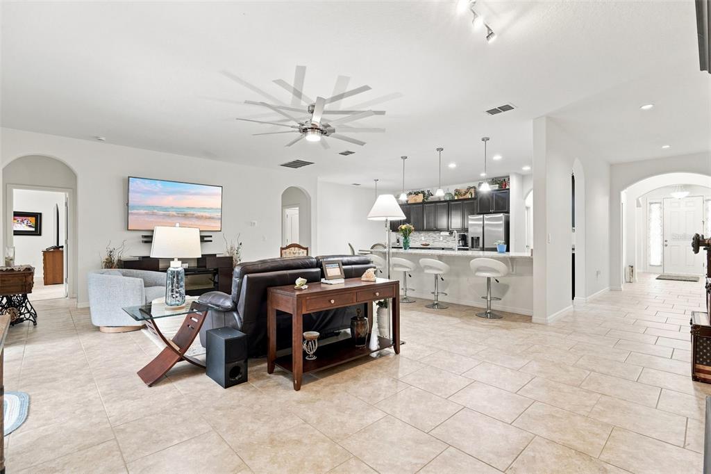 An open-concept living room and kitchen featuring tile floors, a ceiling fan, and bar seating — 517 MORGAN WOOD DRIVE, DELAND, FL