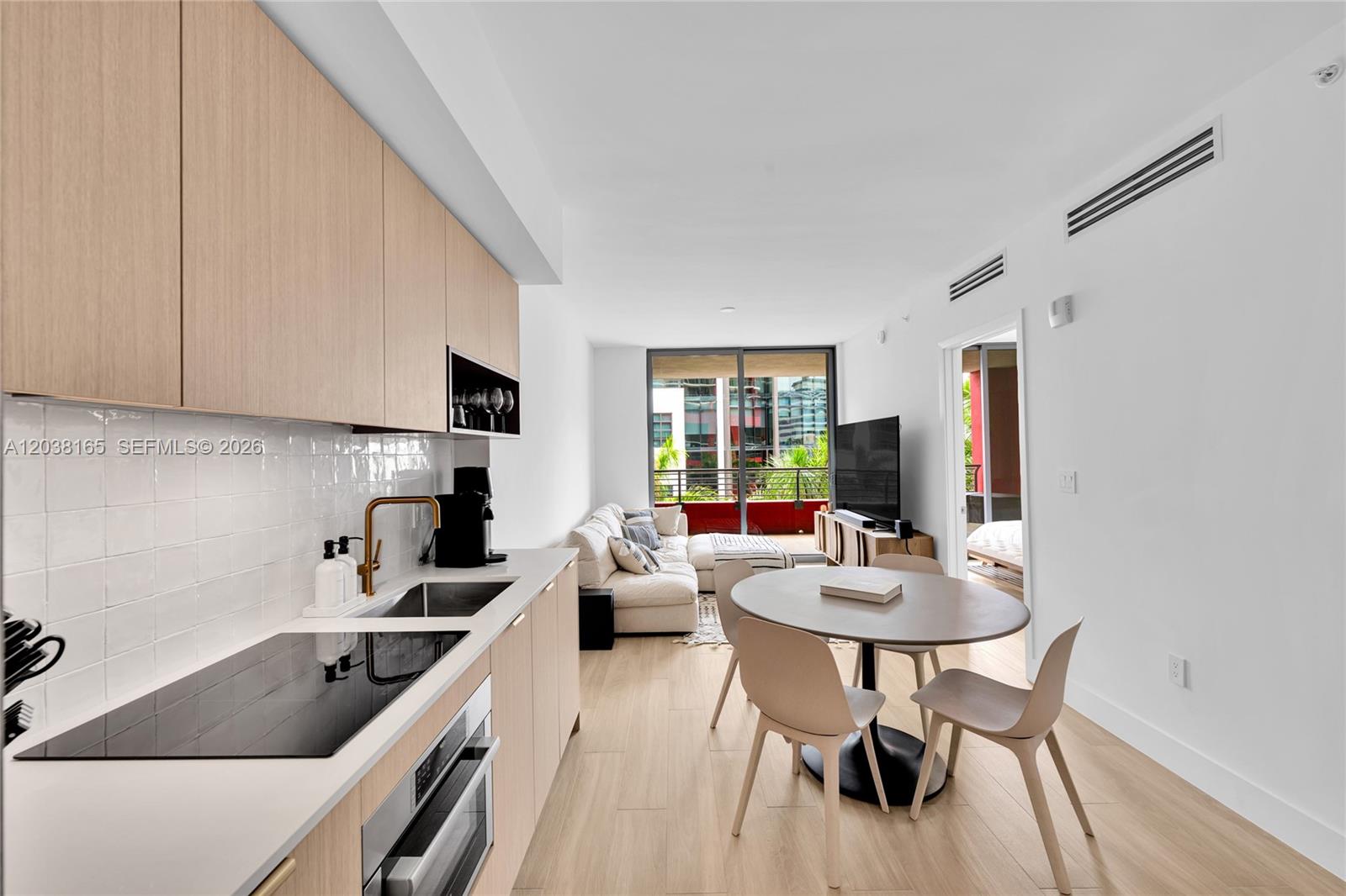 A modern kitchen flows into a dining area and living room with a balcony view — 90 NE 32nd # 406, Miami FL 33127, MIAMI, FL