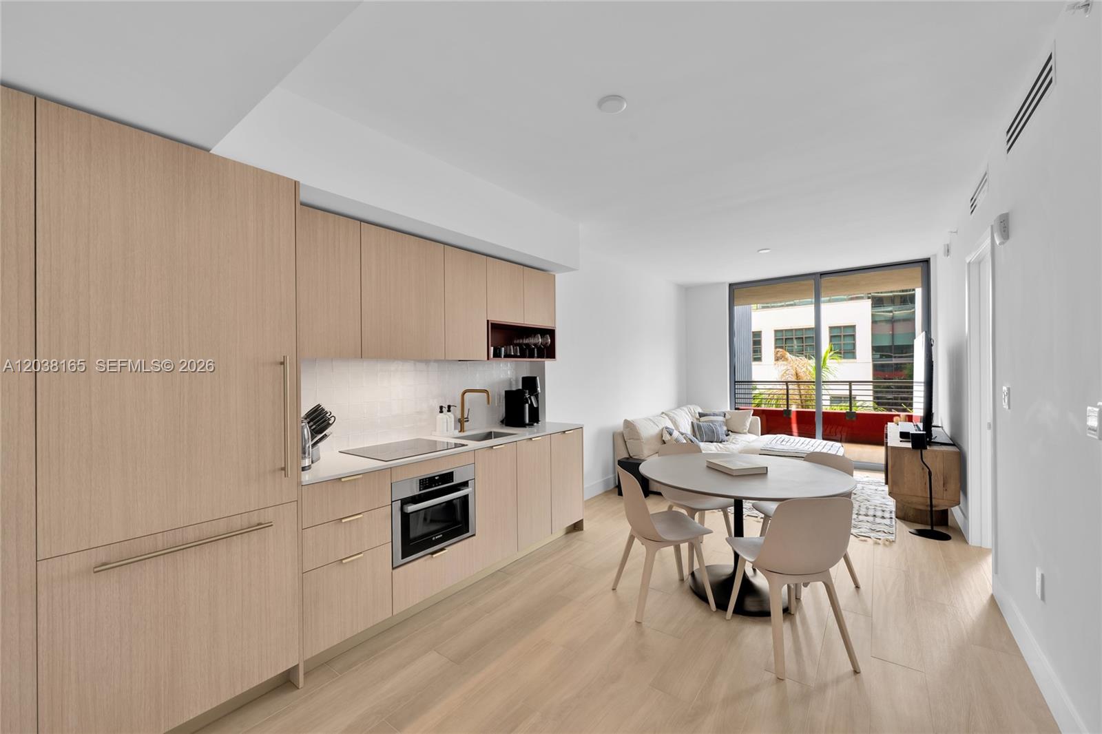 A modern kitchen with light wood cabinetry and a dining area opens to a balcony — 90 NE 32nd # 406, Miami FL 33127, MIAMI, FL