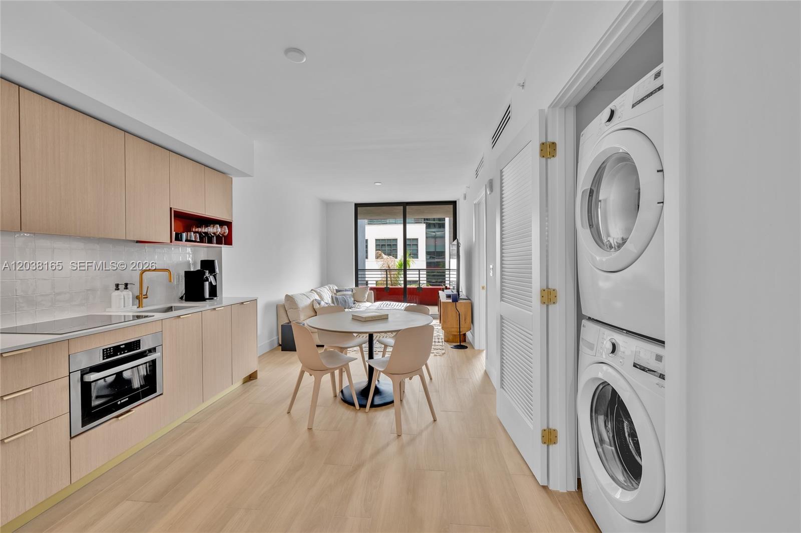 A modern kitchen and dining area features light wood cabinetry, a stacked washer-dryer, and balcony access — 90 NE 32nd # 406, Miami FL 33127, MIAMI, FL
