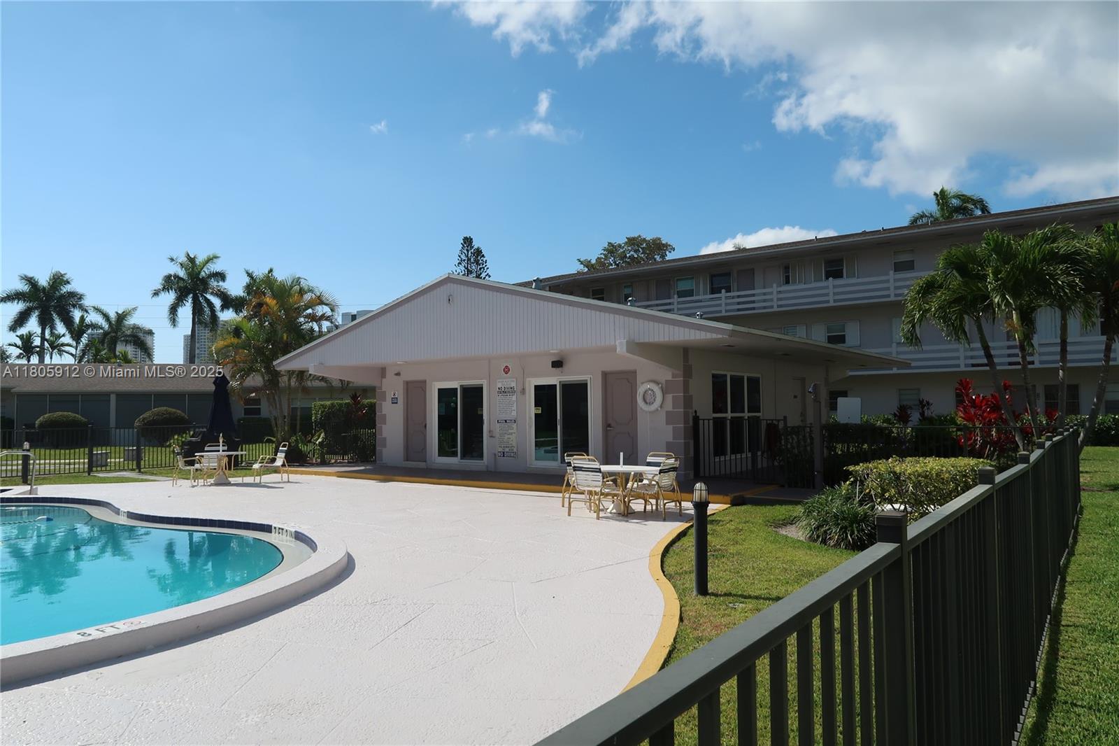 A swimming pool sits on a patio in front of a clubhouse and apartment building — 700 Layne Blvd # 112, Hallandale Beach FL 33009, HALLANDALE BEACH, FL