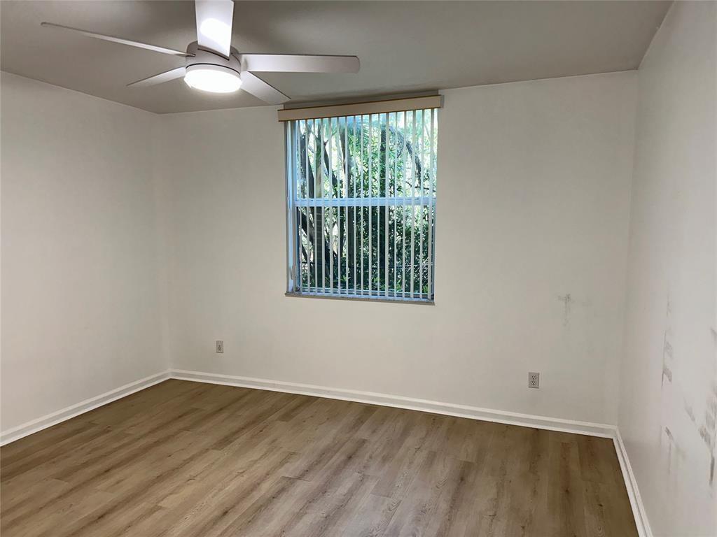 An empty bedroom features light wood-look flooring, white walls, a ceiling fan, and vertical blinds — 529 E Sheridan Street # 1081, Dania Beach FL 33004, DANIA BEACH, FL