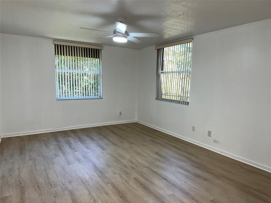 An empty room features light wood-look flooring, white walls, two windows with vertical blinds, and a ceiling fan — 529 E Sheridan Street # 1081, Dania Beach FL 33004, DANIA BEACH, FL