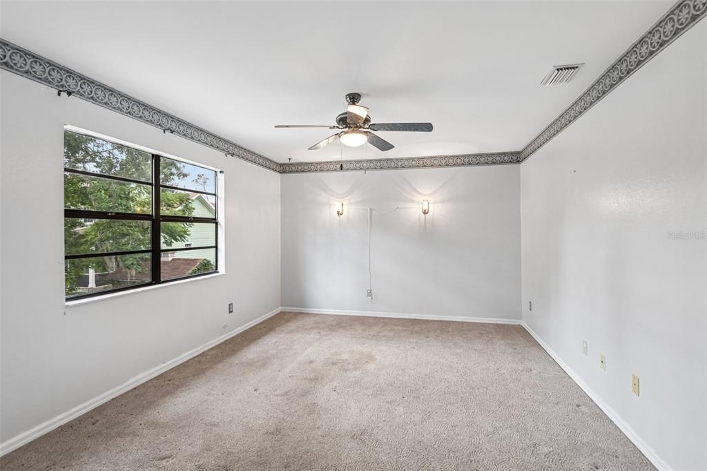 An empty bedroom with beige carpet, a ceiling fan, wall sconces, and a window — 18411 AUTUMN MIST DRIVE, LUTZ, FL
