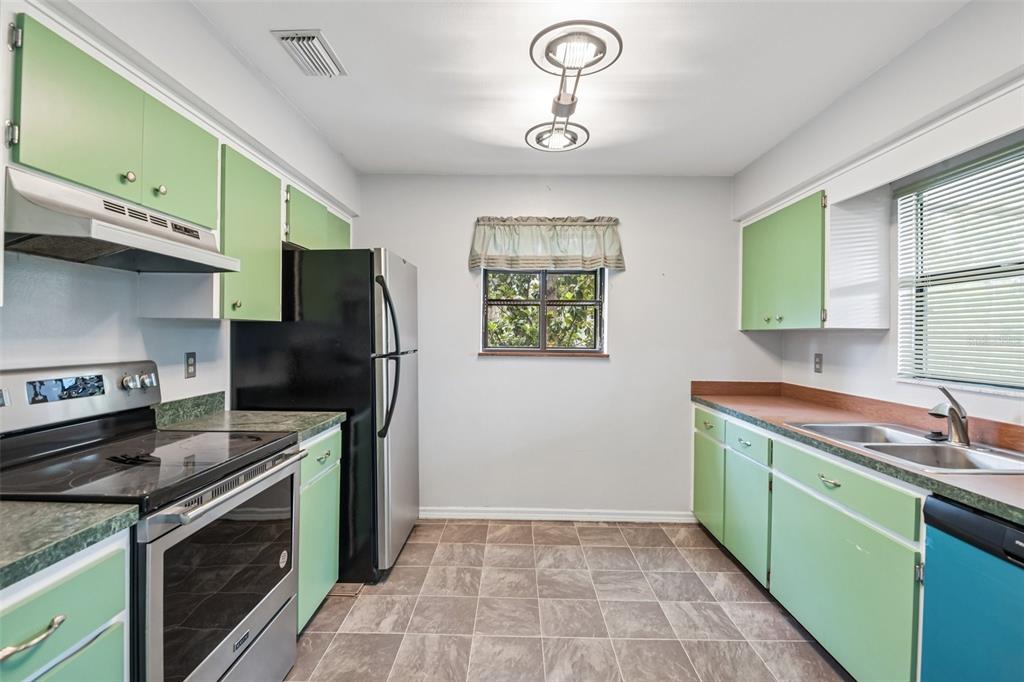 A kitchen features light green cabinets, a black refrigerator, stainless steel appliances, and tiled flooring — 18411 AUTUMN MIST DRIVE, LUTZ, FL
