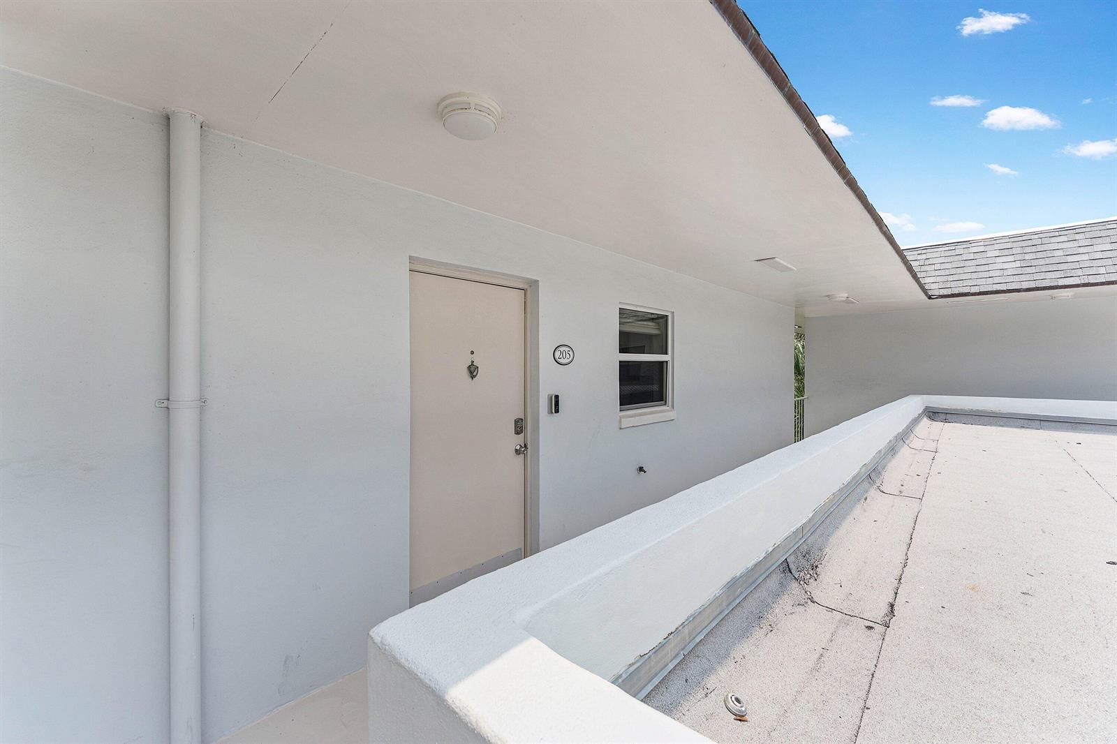 An exterior view of an apartment building walkway with a door labeled 205 — 207 Tropic Isle Drive # 2050, Delray Beach FL 33483, DELRAY BEACH, FL
