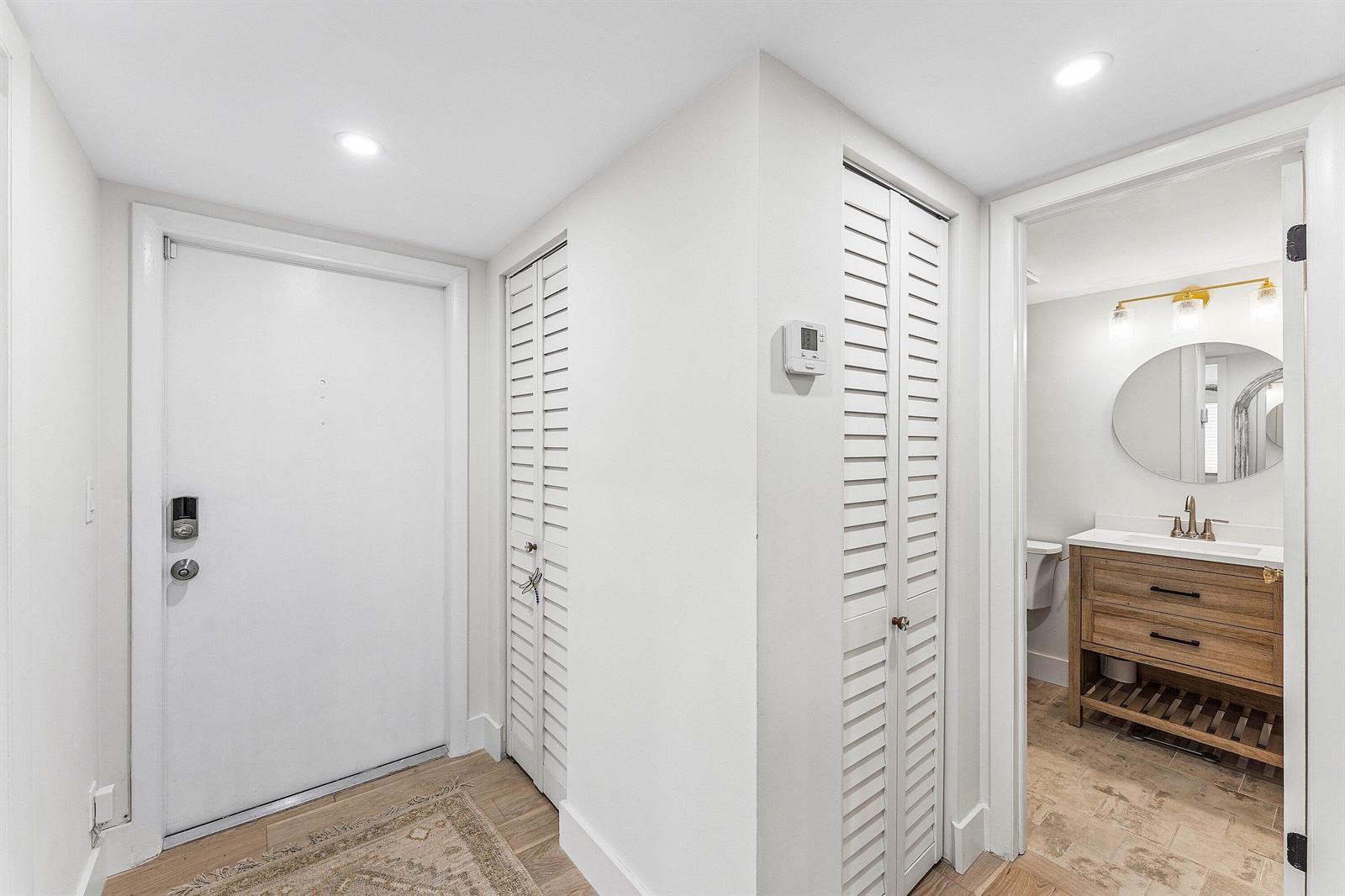 An entryway features a white door, two louvered closets, and a doorway leading to a bathroom — 207 Tropic Isle Drive # 2050, Delray Beach FL 33483, DELRAY BEACH, FL