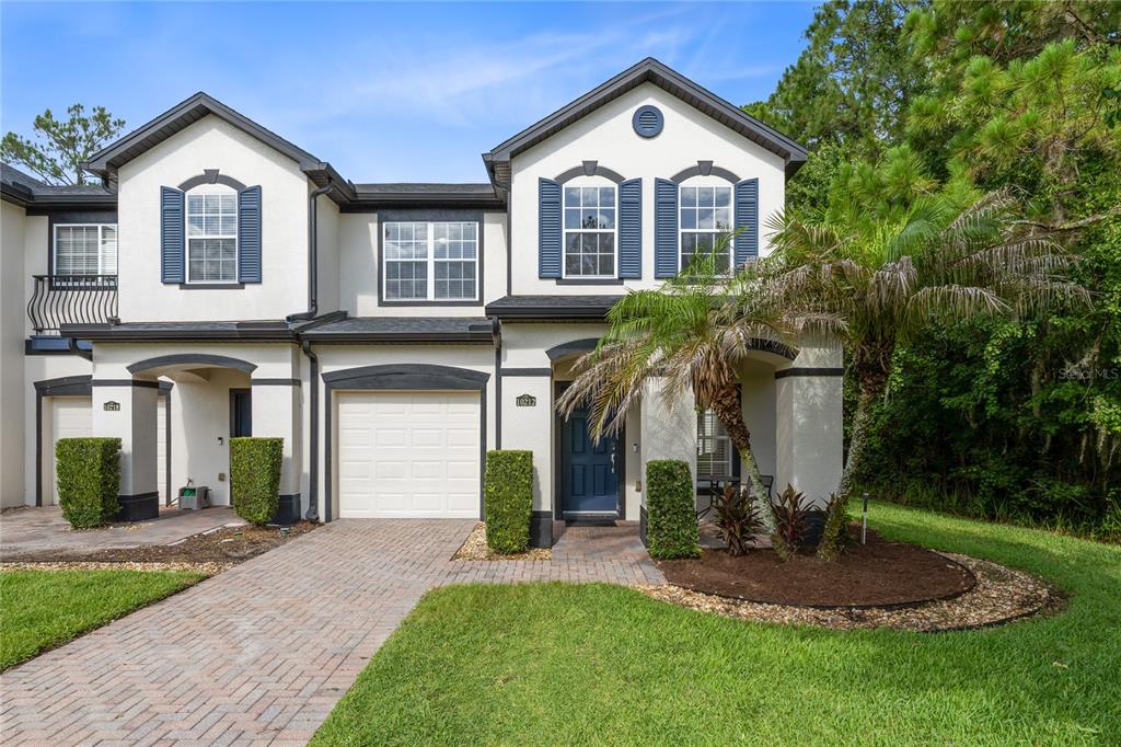 A two-story townhouse with a white stucco facade, blue shutters, and a brick driveway — 10212 PARK COMMONS DRIVE, ORLANDO, FL
