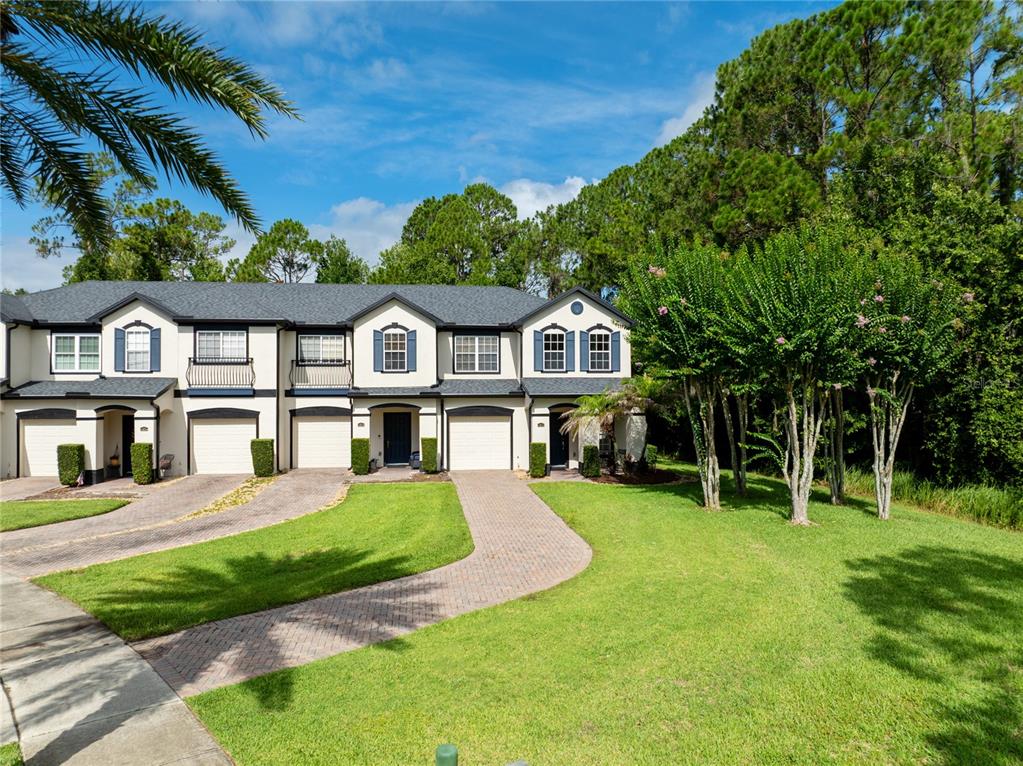 A row of two-story townhomes with attached garages and paved driveways sits beside green trees — 10212 PARK COMMONS DRIVE, ORLANDO, FL