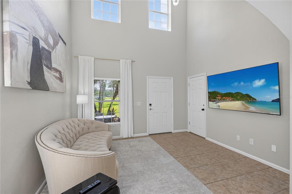 A living room features a curved sofa, a wall-mounted television, and high ceilings with windows — 10212 PARK COMMONS DRIVE, ORLANDO, FL