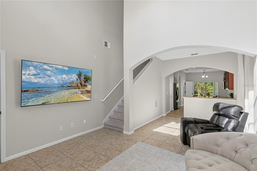 A living room features a wall-mounted television, tiled floors, a staircase, and an arched entryway — 10212 PARK COMMONS DRIVE, ORLANDO, FL