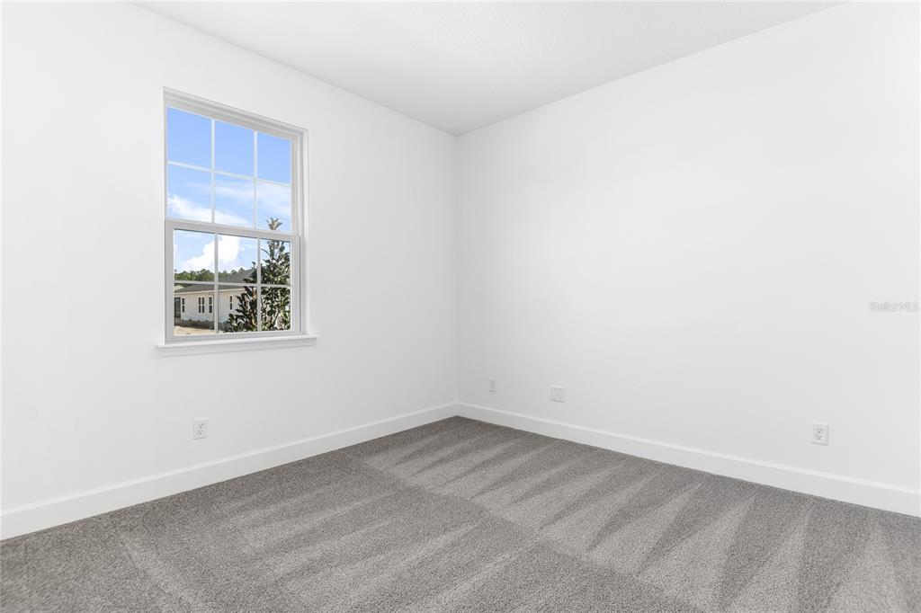 A bedroom with white walls, gray carpet, and a single window overlooking an exterior view — 196 ENCLAVE AVENUE, PALM COAST, FL