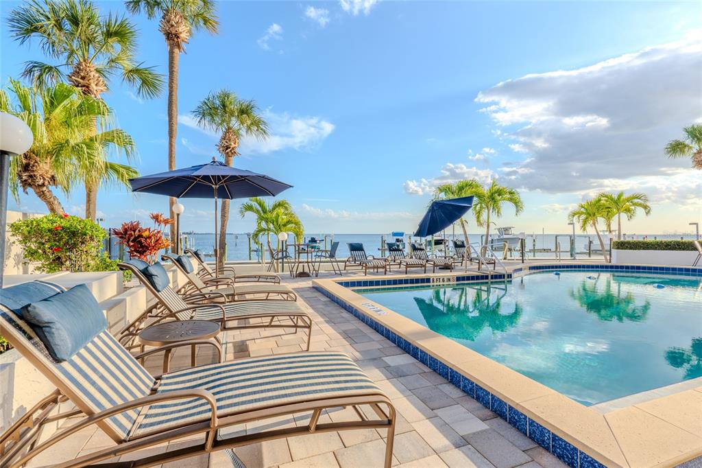 A swimming pool with lounge chairs and umbrellas overlooks the ocean on a sunny day — 5700 MARINER STREET UNIT 503A, TAMPA, FL