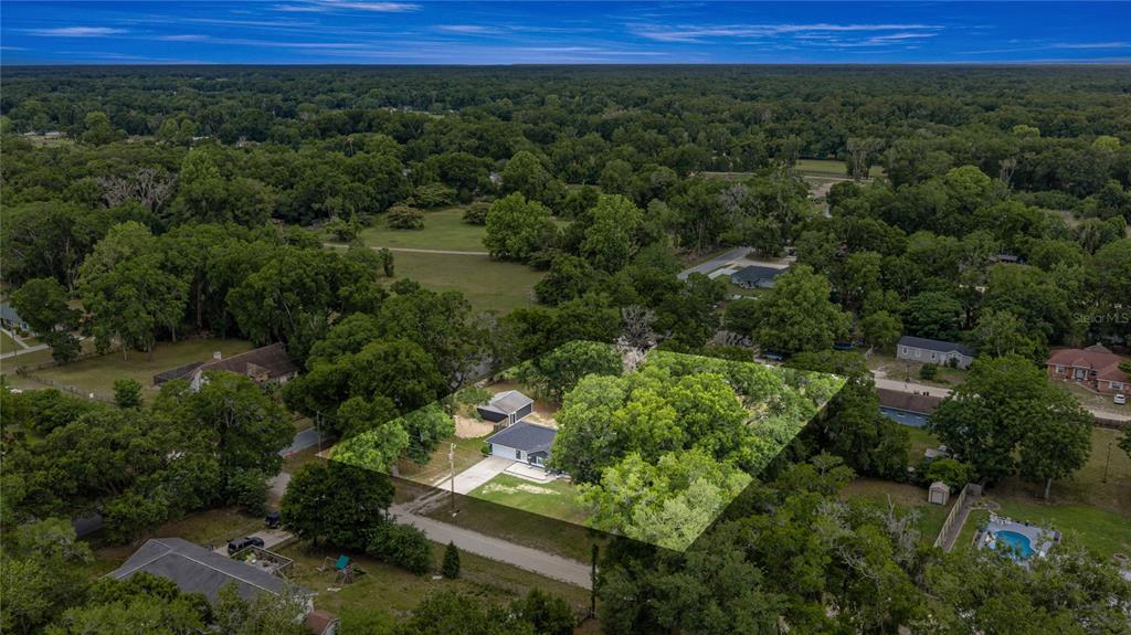 An aerial view shows a single-story house surrounded by dense trees on a residential lot — 13980 SE 53RD AVENUE, SUMMERFIELD, FL