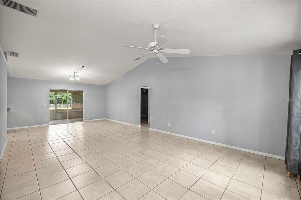 A spacious living area features light gray walls, tile flooring, a vaulted ceiling, and sliding doors — 13980 SE 53RD AVENUE, SUMMERFIELD, FL