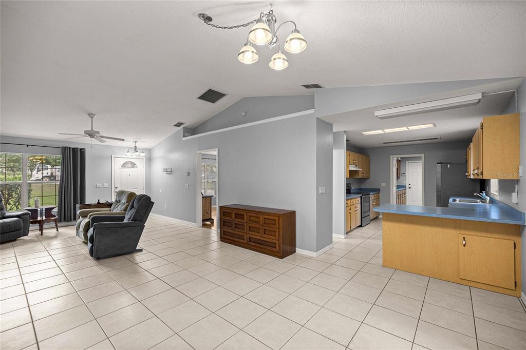 An open-concept living room and kitchen with light tile flooring and vaulted ceilings — 13980 SE 53RD AVENUE, SUMMERFIELD, FL