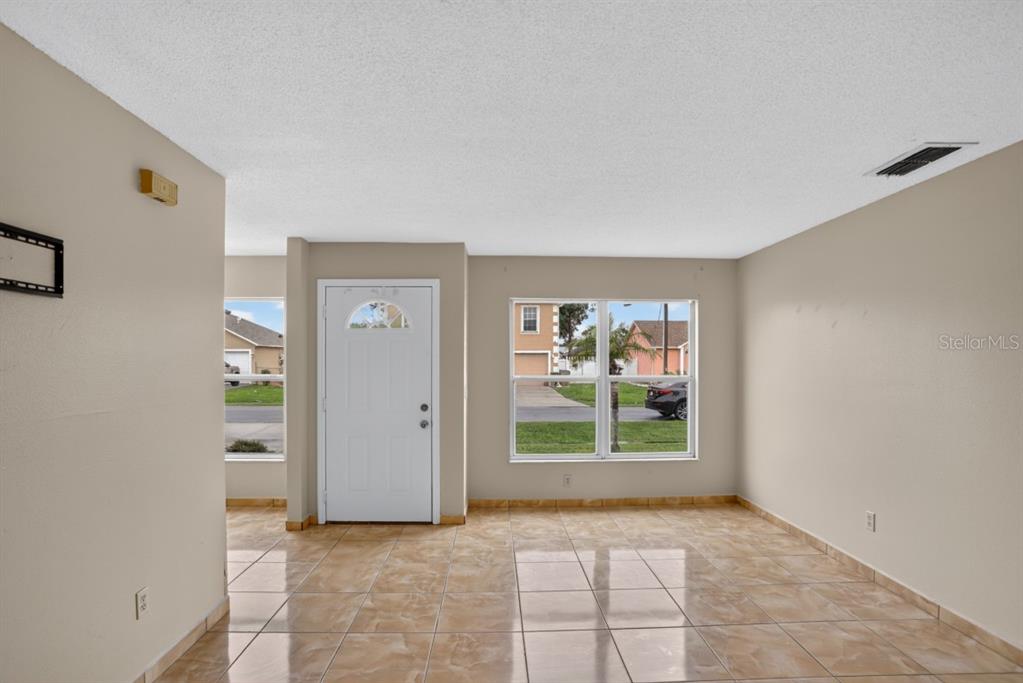 An empty room with beige walls, tile flooring, a white front door, and two windows — 145 DORCHESTER COURT, KISSIMMEE, FL