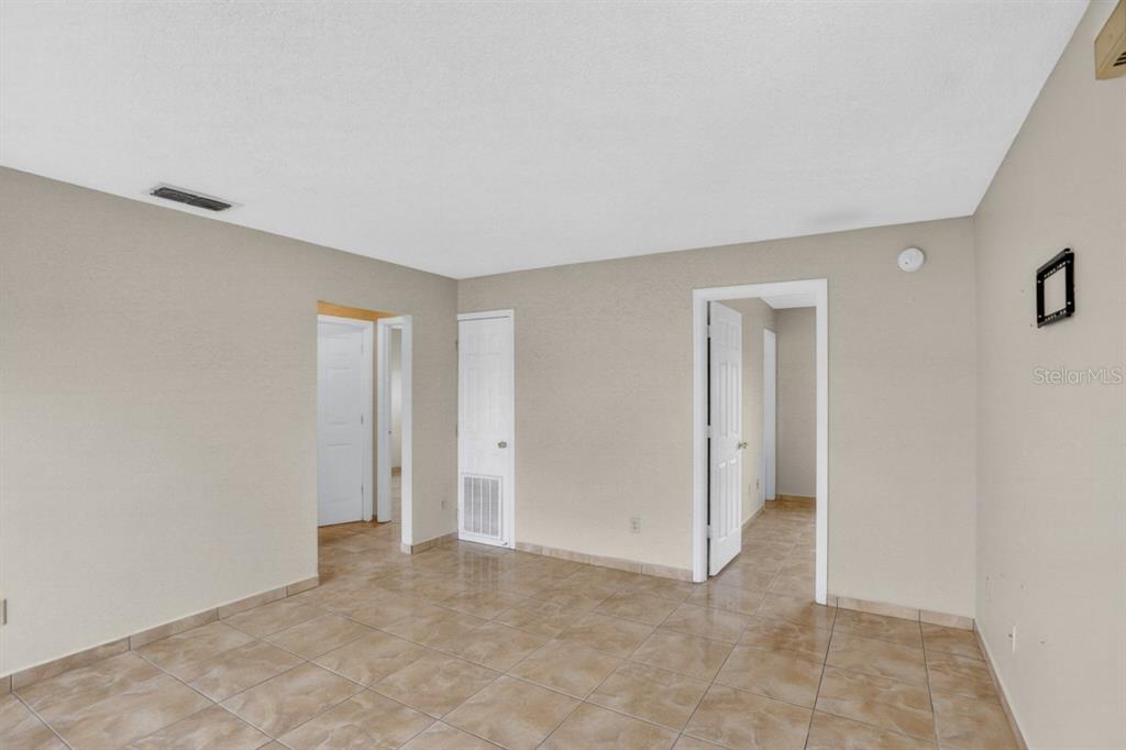 An empty room features beige walls, light-colored tile flooring, and two doorways leading to other areas — 145 DORCHESTER COURT, KISSIMMEE, FL