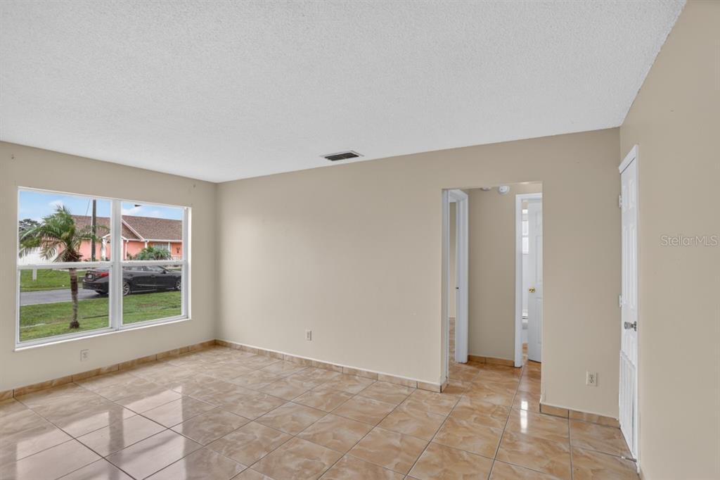 An empty room with tan walls, light-colored tile flooring, and a window overlooking a street — 145 DORCHESTER COURT, KISSIMMEE, FL