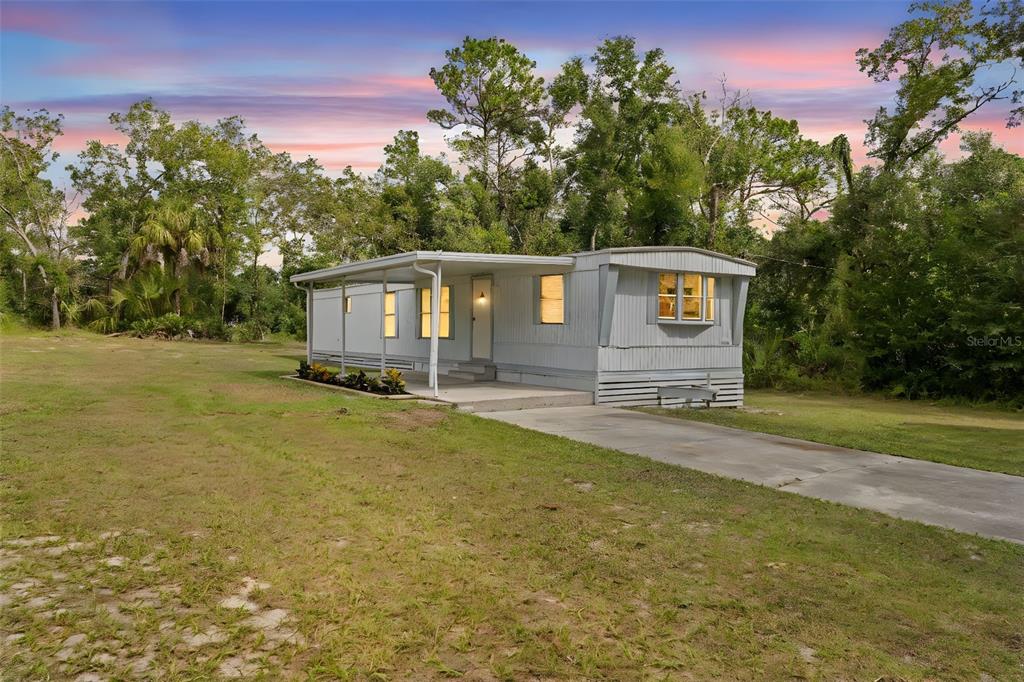 A light-colored mobile home with a covered porch sits on a grassy lot — 8061 W ROSELLA COURT, CRYSTAL RIVER, FL