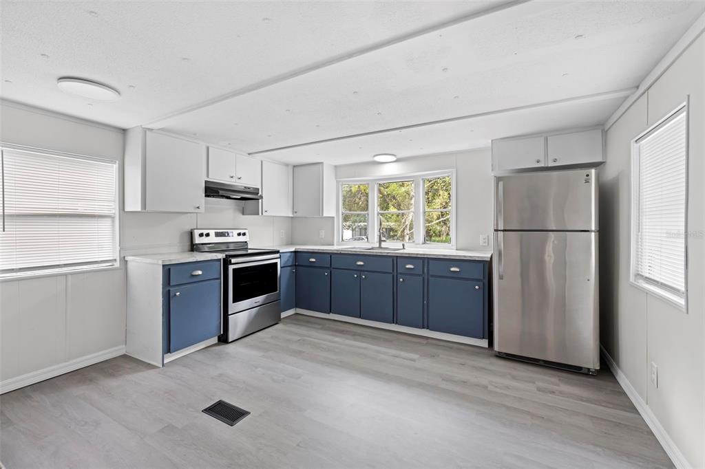 A kitchen features blue lower cabinets, white upper cabinets, stainless steel appliances, and wood-look flooring — 8061 W ROSELLA COURT, CRYSTAL RIVER, FL
