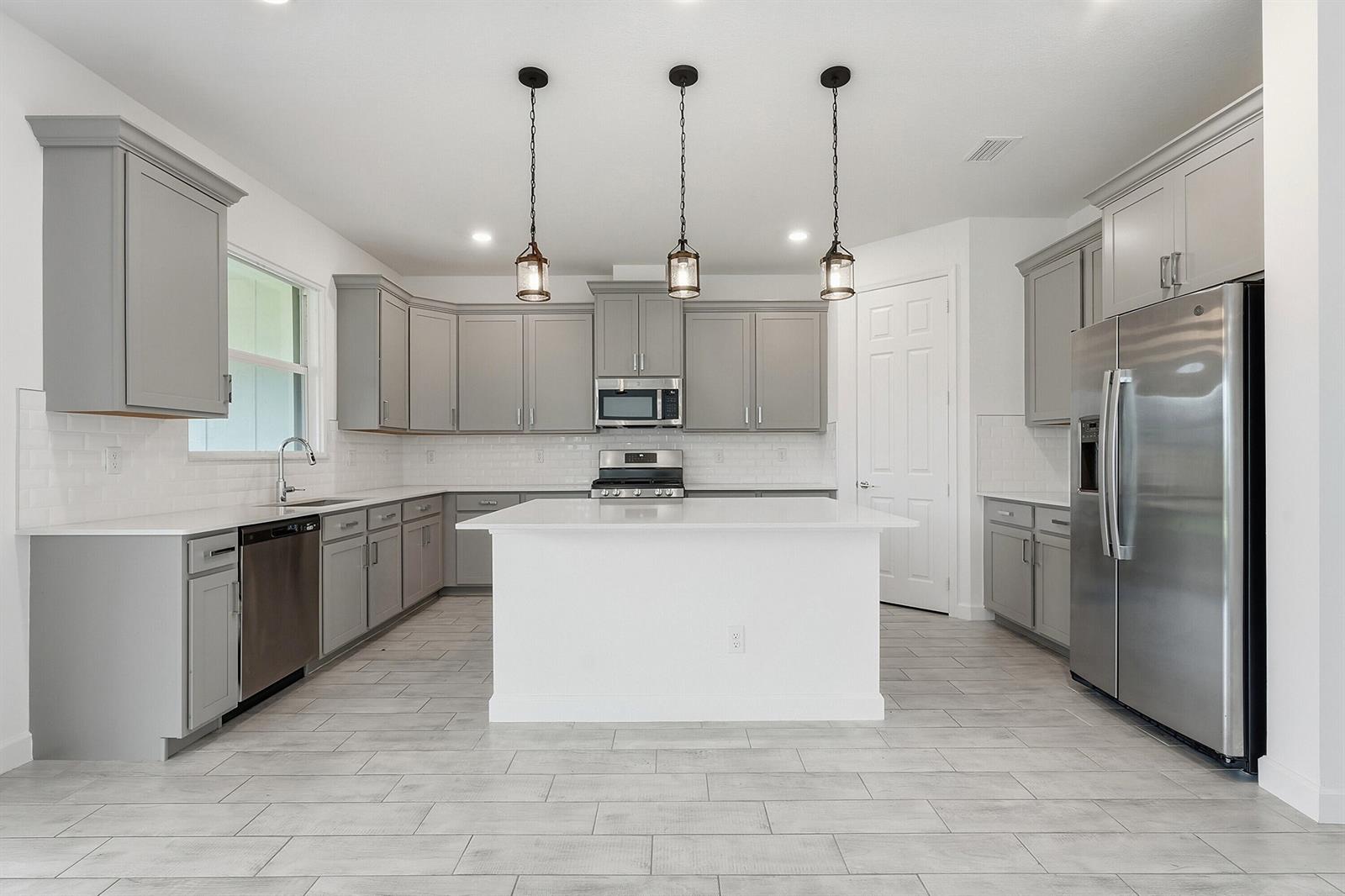 A kitchen features gray cabinets, white countertops, a central island, and stainless steel appliances — 1261 Deer Hvn Drive, Loxahatchee FL 33470, LOXAHATCHEE, FL