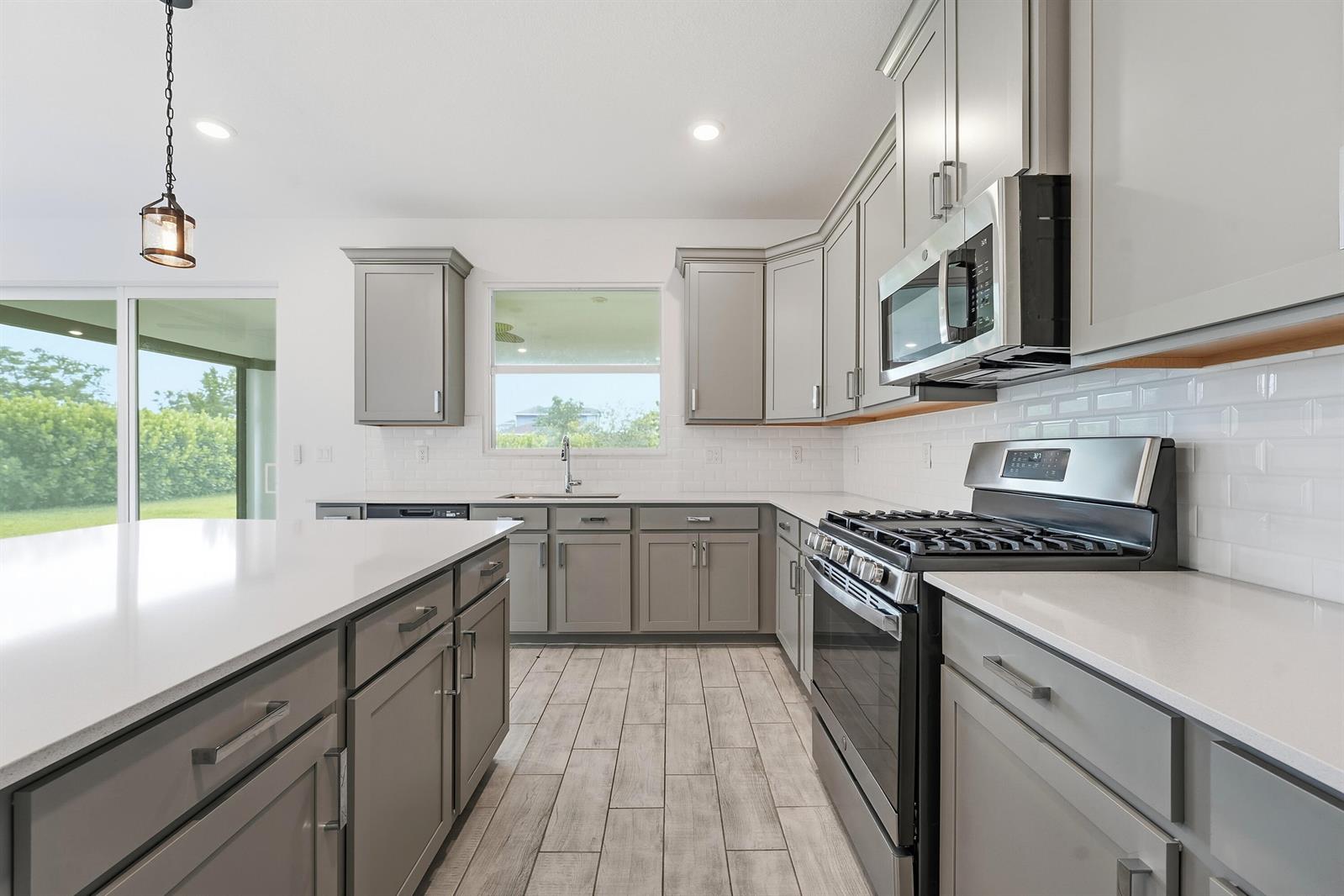 A modern kitchen features gray cabinets, white quartz countertops, stainless steel appliances, and tile flooring — 1261 Deer Hvn Drive, Loxahatchee FL 33470, LOXAHATCHEE, FL