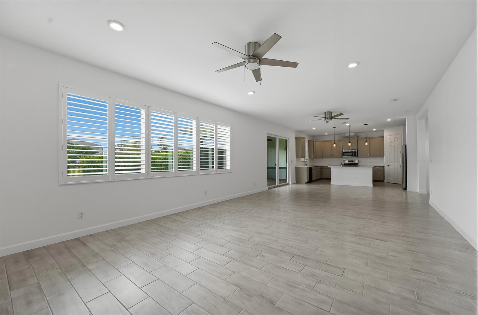 An open-concept living area features light wood-look tile flooring, white walls, and a modern kitchen — 1261 Deer Hvn Drive, Loxahatchee FL 33470, LOXAHATCHEE, FL