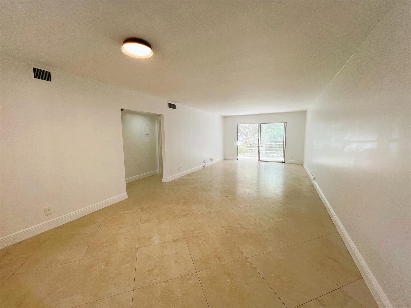 An empty living room features white walls, beige tile flooring, and a sliding glass door — 3001 Portofino Isle # E2, Coconut Creek FL 33066, COCONUT CREEK, FL