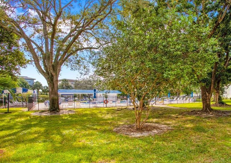 A grassy lawn with trees leads to a fenced swimming pool area with a pavilion — 3001 Portofino Isle # E2, Coconut Creek FL 33066, COCONUT CREEK, FL