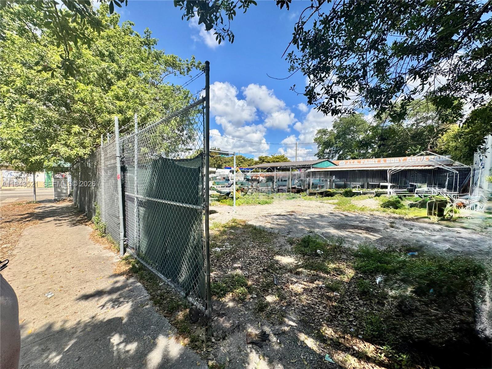 A chain-link fence borders a vacant, unpaved lot next to an auto body shop — 6501 NW 7th Ave, Miami FL 33150, MIAMI, FL