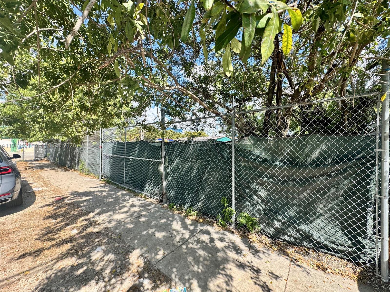 A chain-link fence with a privacy screen runs along a concrete sidewalk under trees — 6501 NW 7th Ave, Miami FL 33150, MIAMI, FL