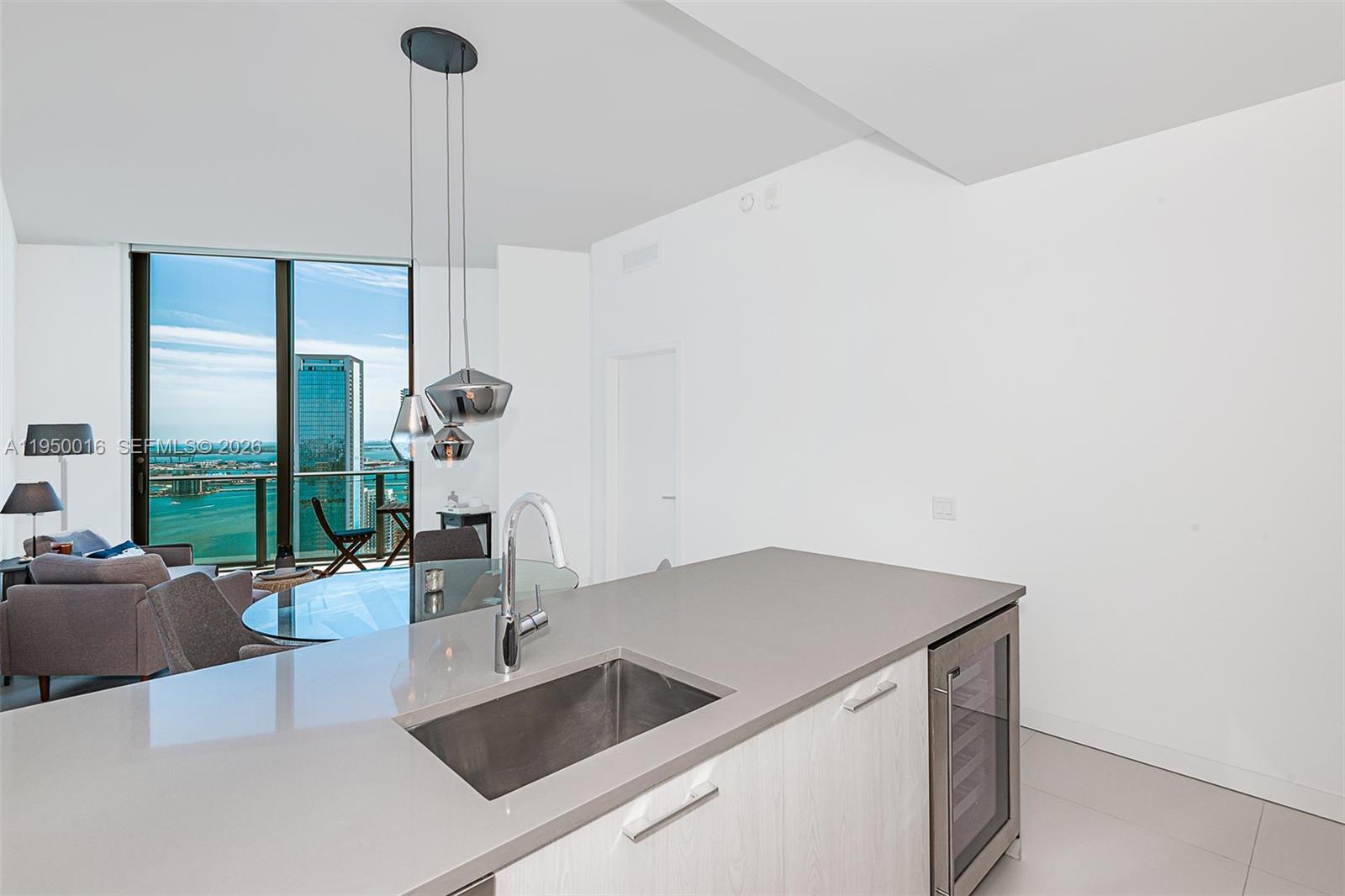 A modern kitchen island with a sink and wine cooler overlooks a dining area — 501 NE 31st St, Miami FL 33137, MIAMI, FL
