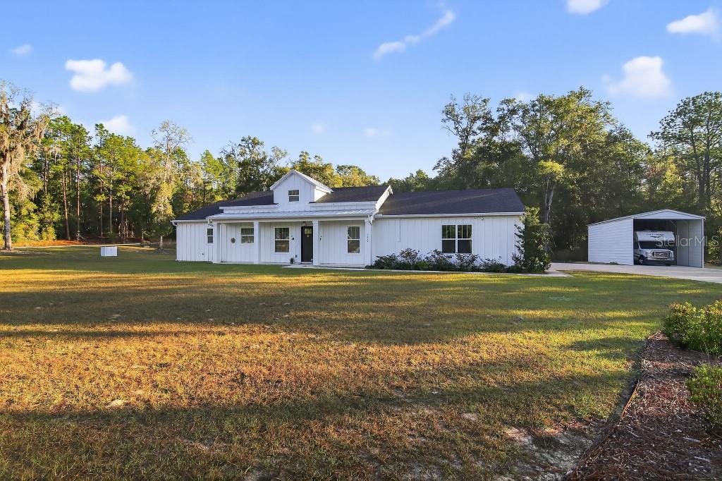 A white farmhouse with a metal roof and a detached garage sits on a lawn — 5859 SW 129TH TERRACE ROAD, OCALA, FL