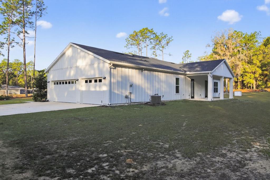 A white, modern farmhouse-style home with a two-car garage and a covered side porch — 5859 SW 129TH TERRACE ROAD, OCALA, FL