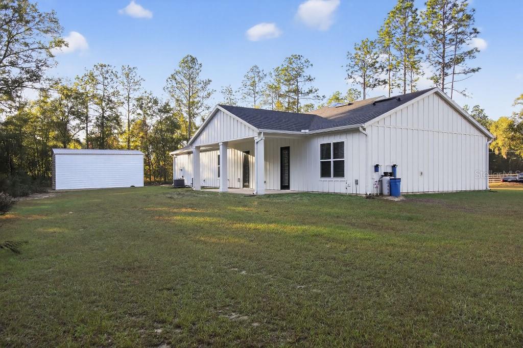 A white farmhouse-style house with a covered patio and a detached shed in the backyard — 5859 SW 129TH TERRACE ROAD, OCALA, FL