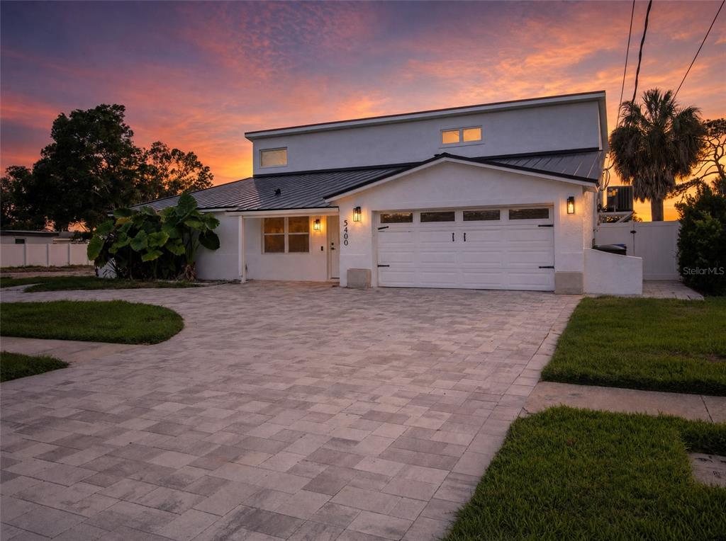 A white house with a metal roof and a paved driveway stands at sunset — 5400 DENVER STREET NE, ST PETERSBURG, FL