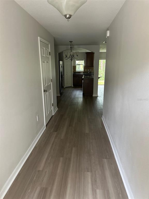 A hallway with light wood-look flooring leads toward a kitchen with dark cabinetry — 2800 BIRCHCREEK DRIVE, WESLEY CHAPEL, FL