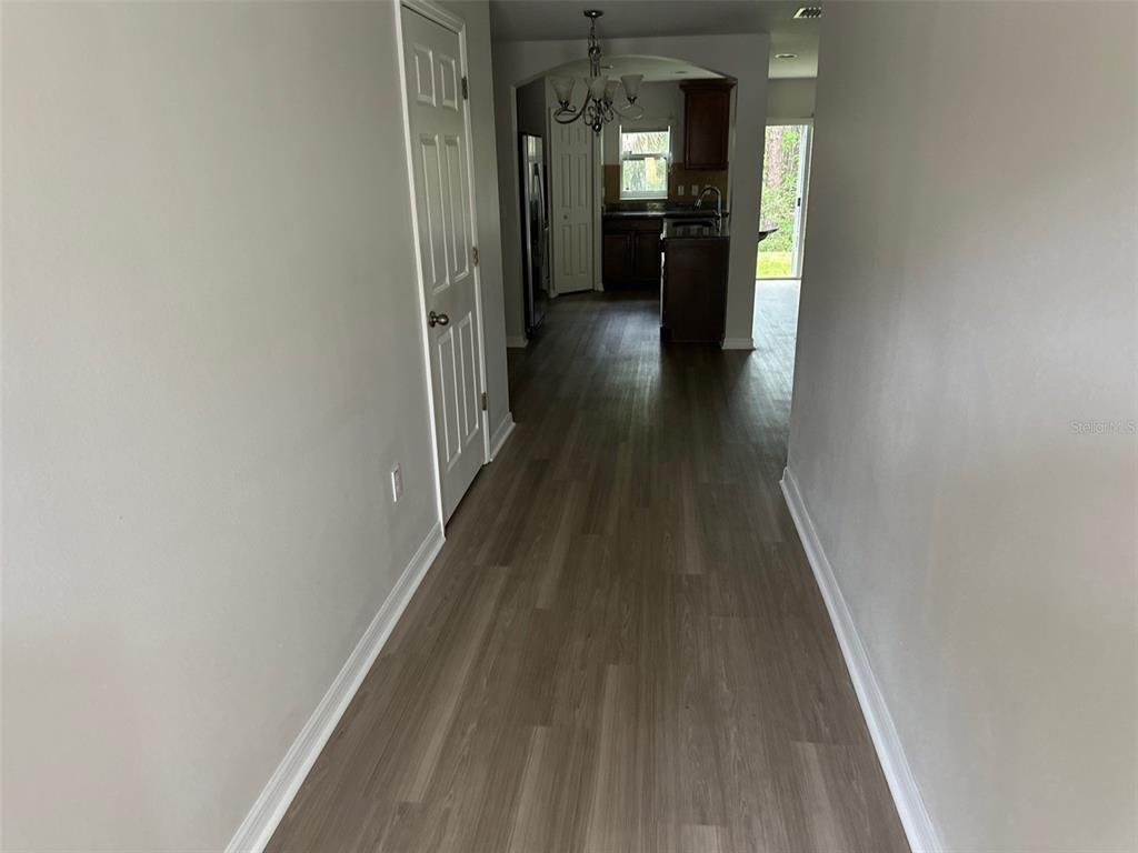 A hallway with light wood-look flooring leads toward a kitchen with dark cabinetry — 2800 BIRCHCREEK DRIVE, WESLEY CHAPEL, FL