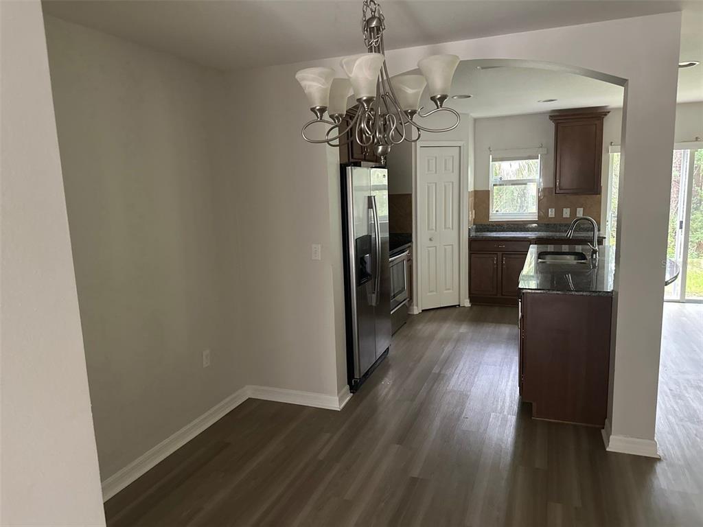 A dining area with a chandelier leads into a kitchen featuring dark cabinets and appliances — 2800 BIRCHCREEK DRIVE, WESLEY CHAPEL, FL