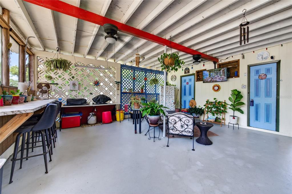 A covered outdoor patio features a bar area, seating, potted plants, and blue doors — 6 HIGHRIDGE ROAD, DAYTONA BEACH, FL