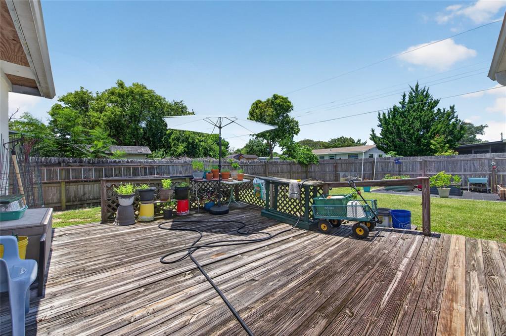 A wooden deck features a patio umbrella, potted plants, and a garden cart in a backyard — 6 HIGHRIDGE ROAD, DAYTONA BEACH, FL