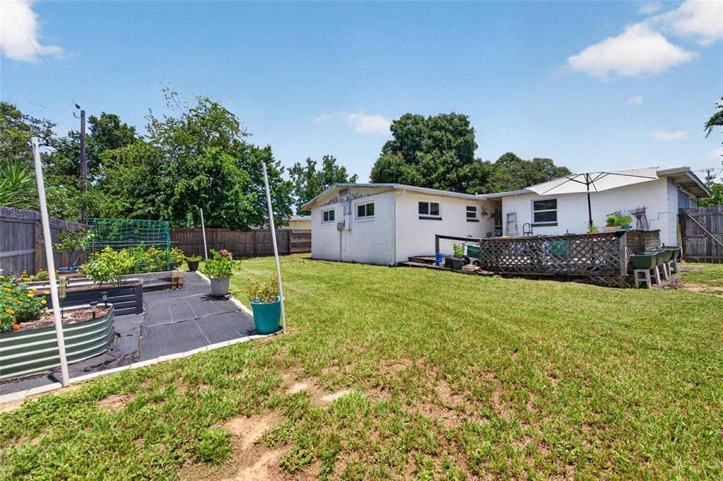 A backyard features a white house with a wooden deck, garden beds, and a fence — 6 HIGHRIDGE ROAD, DAYTONA BEACH, FL