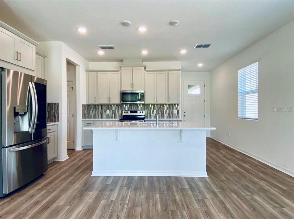 A kitchen features light-colored cabinets, a white island, stainless steel appliances, and wood-look flooring — 2668 SPIDER LILY COURT, CLERMONT, FL